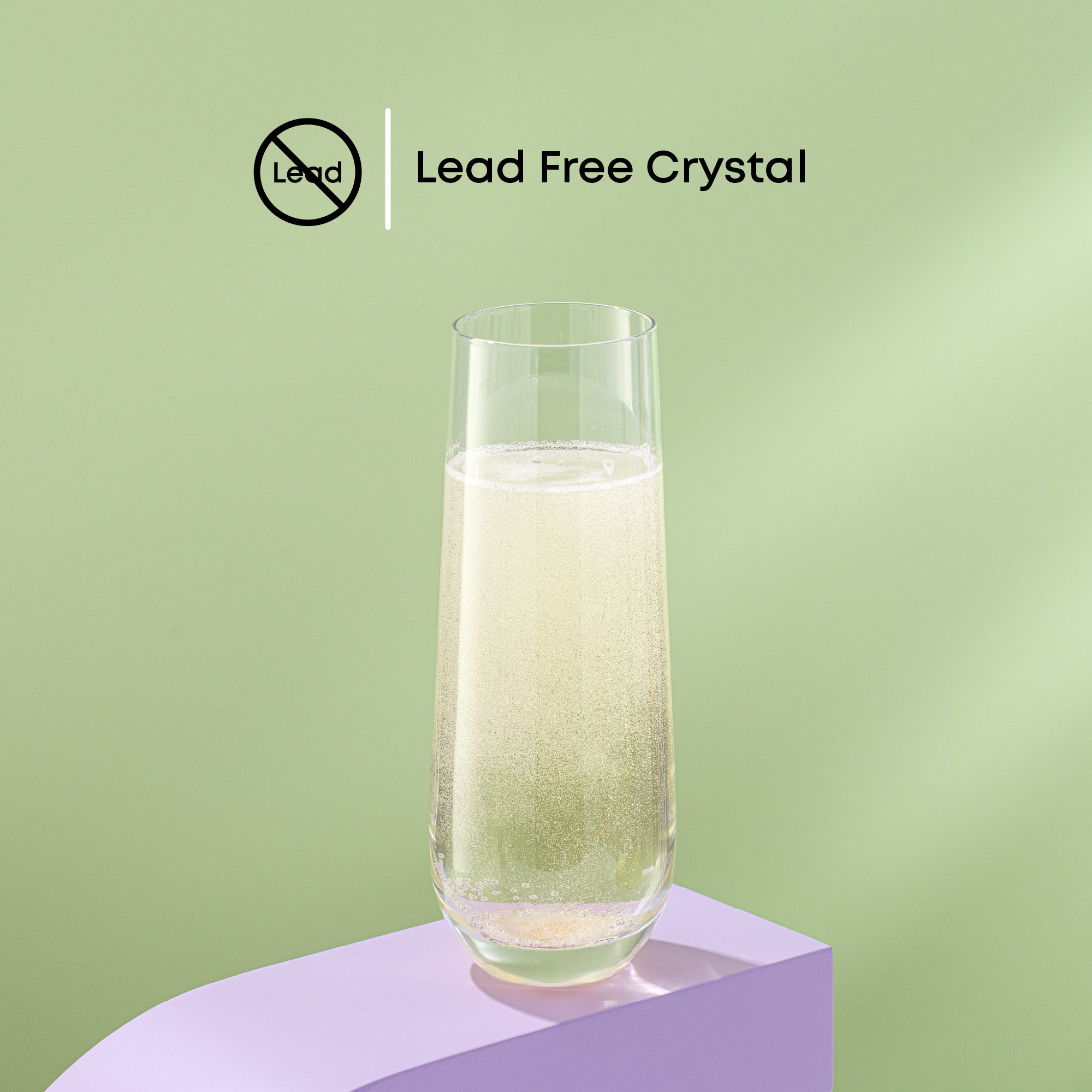 A tall clear glass filled with champagne sits on a purple platform against a green background. Text on the image reads, “Lead Free Crystal.”