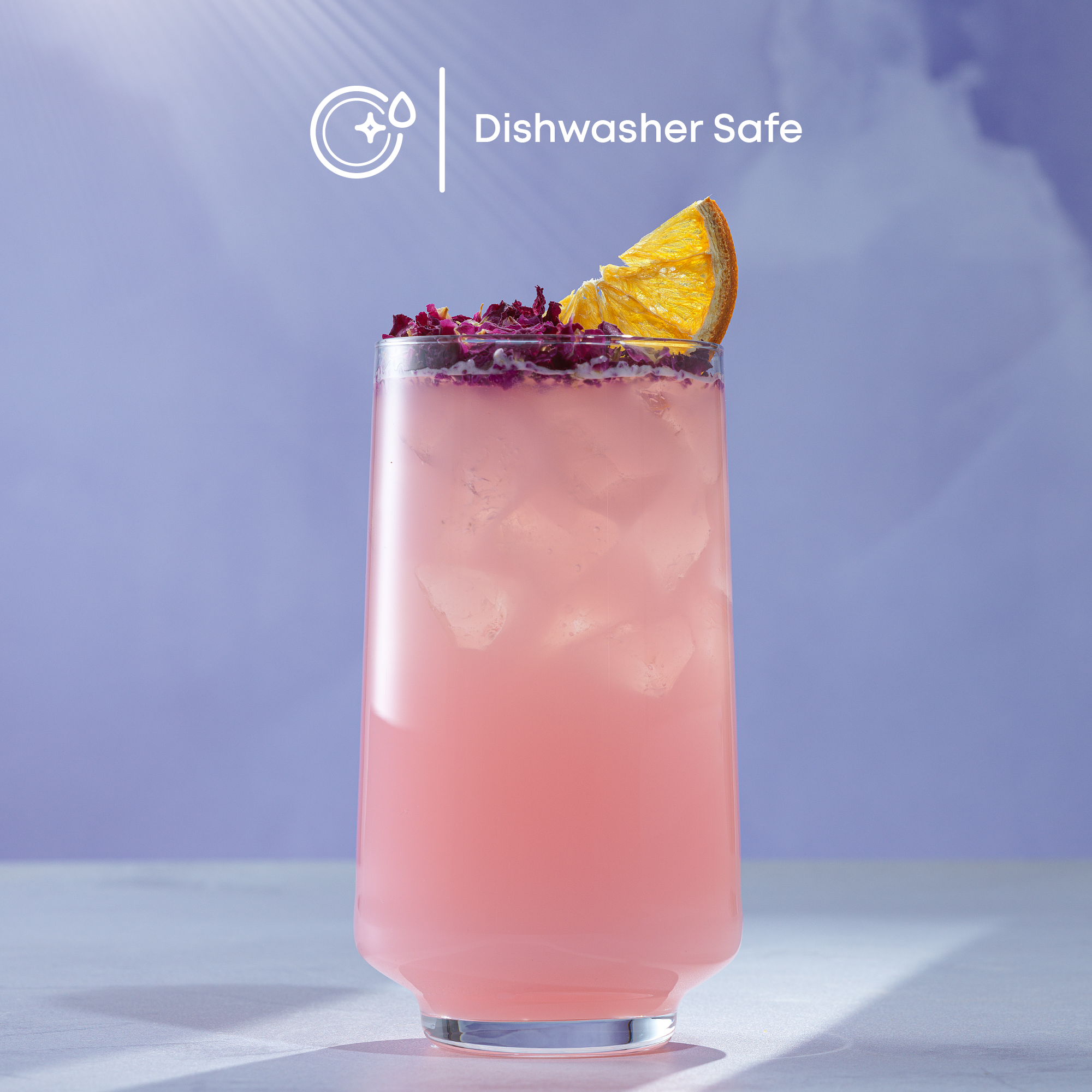 Pink cocktail with lemon wedge and purple flowers in a tall glass on a light surface with a purple gradient background.