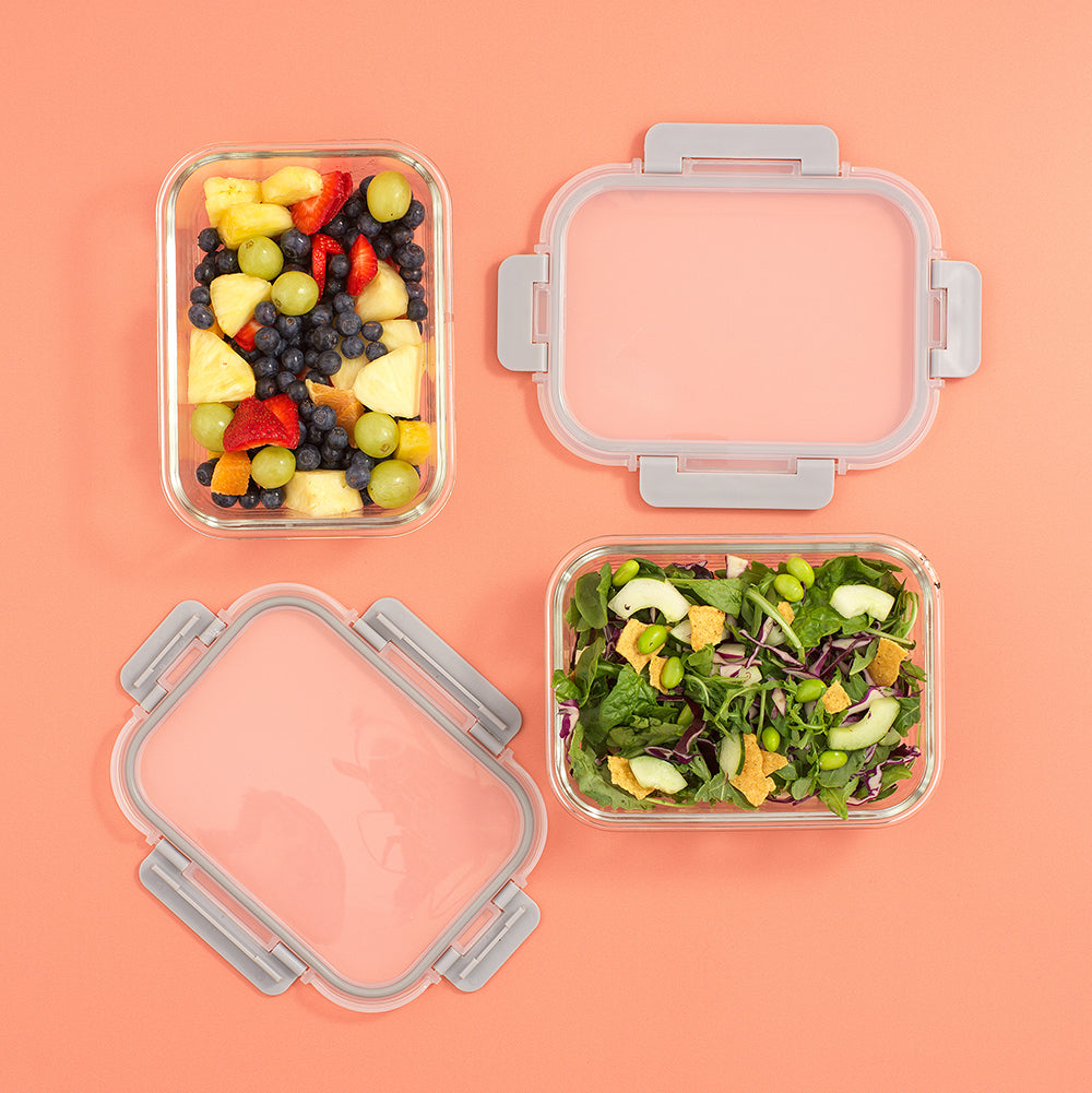 Two containers with food, one containing a salad and the other a mix of fruits and vegetables, on a peach background.