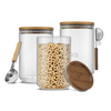 Glass storage canisters with wooden lid and spoon, filled with cereal on a white background.