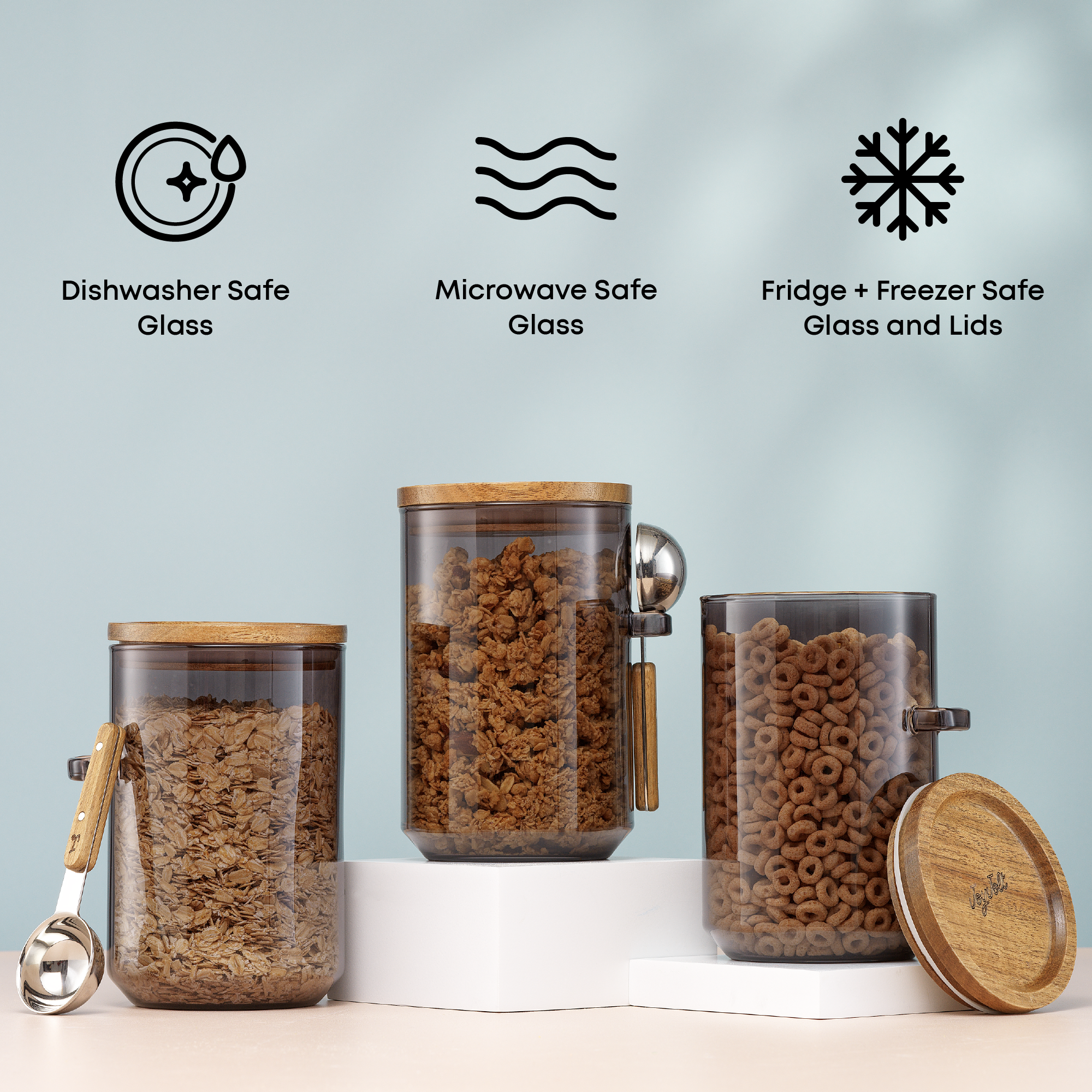 Glass storage jars with wooden lids and measuring spoons on a light blue background with care icons: microwave and dishwasher safe glass, fridge and freezer safe glass and lids.