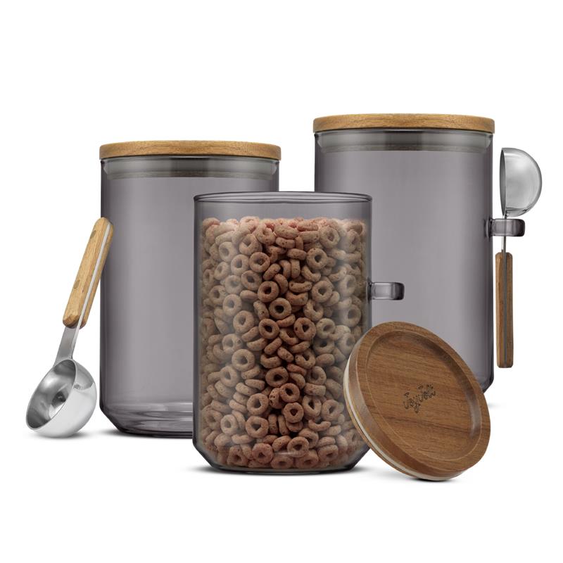 Smoke colored glass storage canisters with wooden lid and spoon, filled with cereal on a white background.