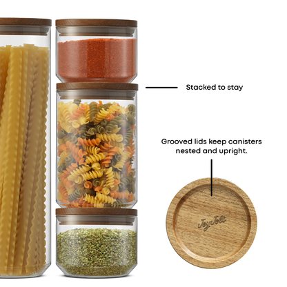 Set of glass jars with wooden lids containing different types of pasta and grains, with text indicating features: "Stacked to stay, grooved lids keep canisters nested and upright"
