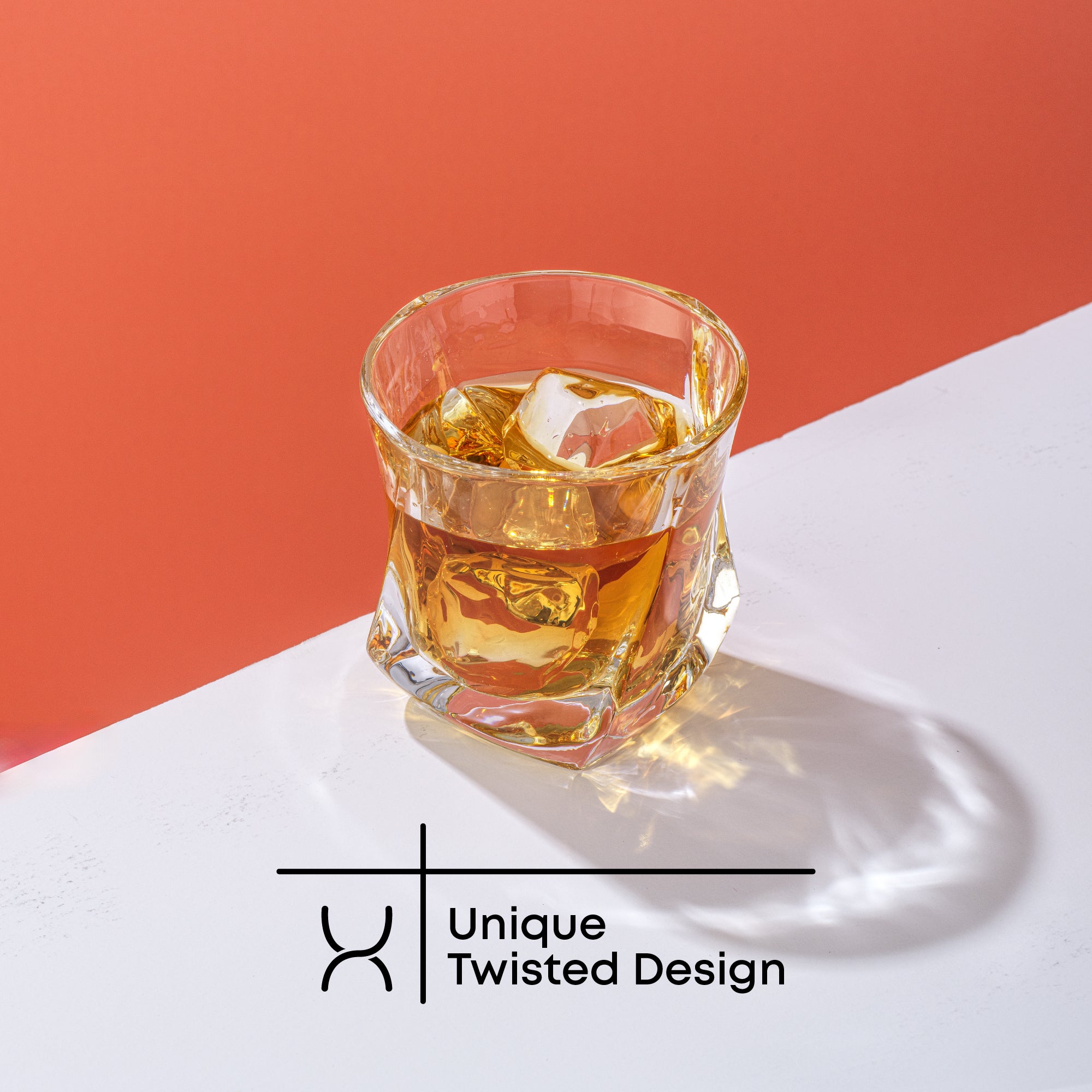 A JoyJolt Aurora Whiskey glass filled with whiskey and ice on a red and white background. Text on image reads, “Unique Twisted Design.”