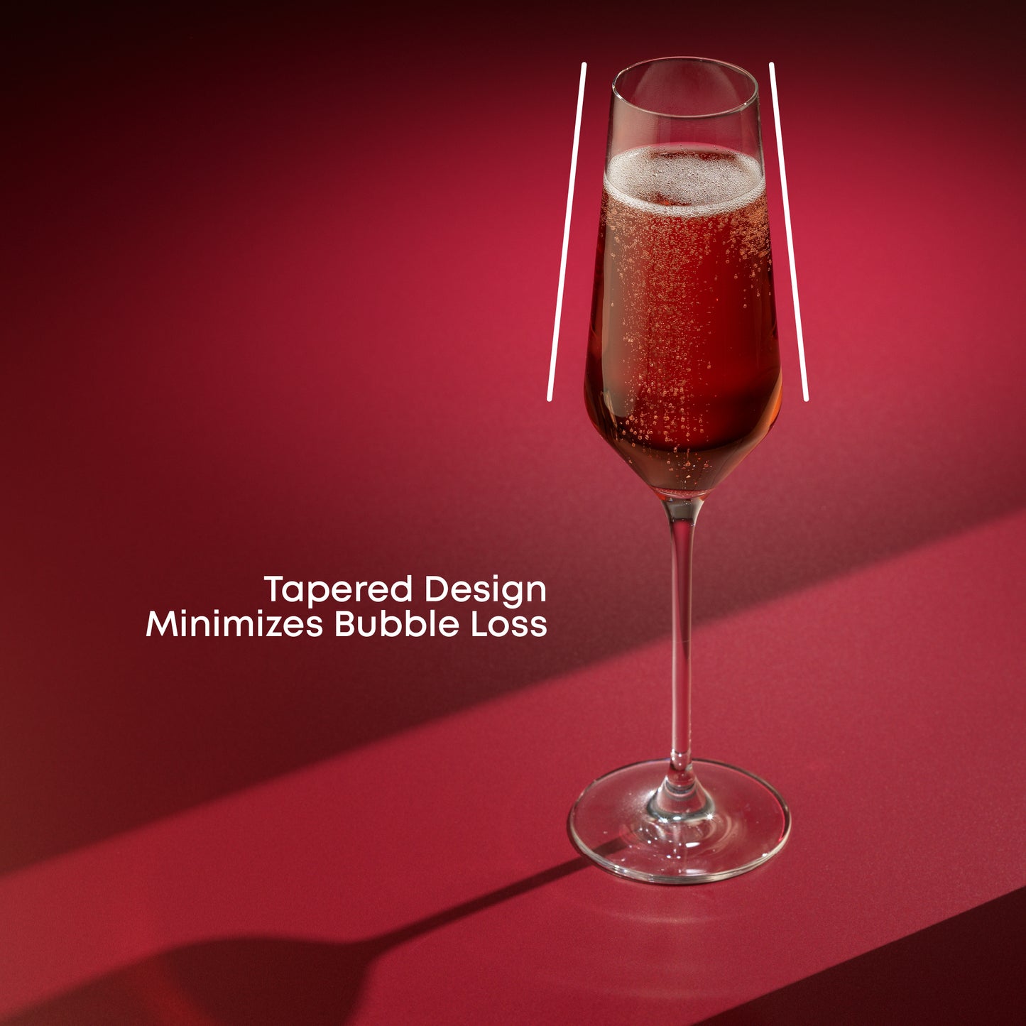 A champagne glass full of champagne on a red surface against a red background with text saying tapered design minimizes bubble loss