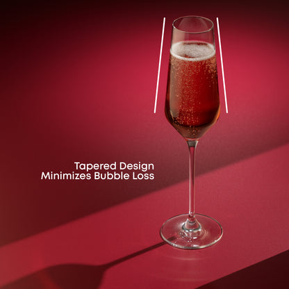 A champagne glass full of champagne on a red surface against a red background with text saying tapered design minimizes bubble loss
