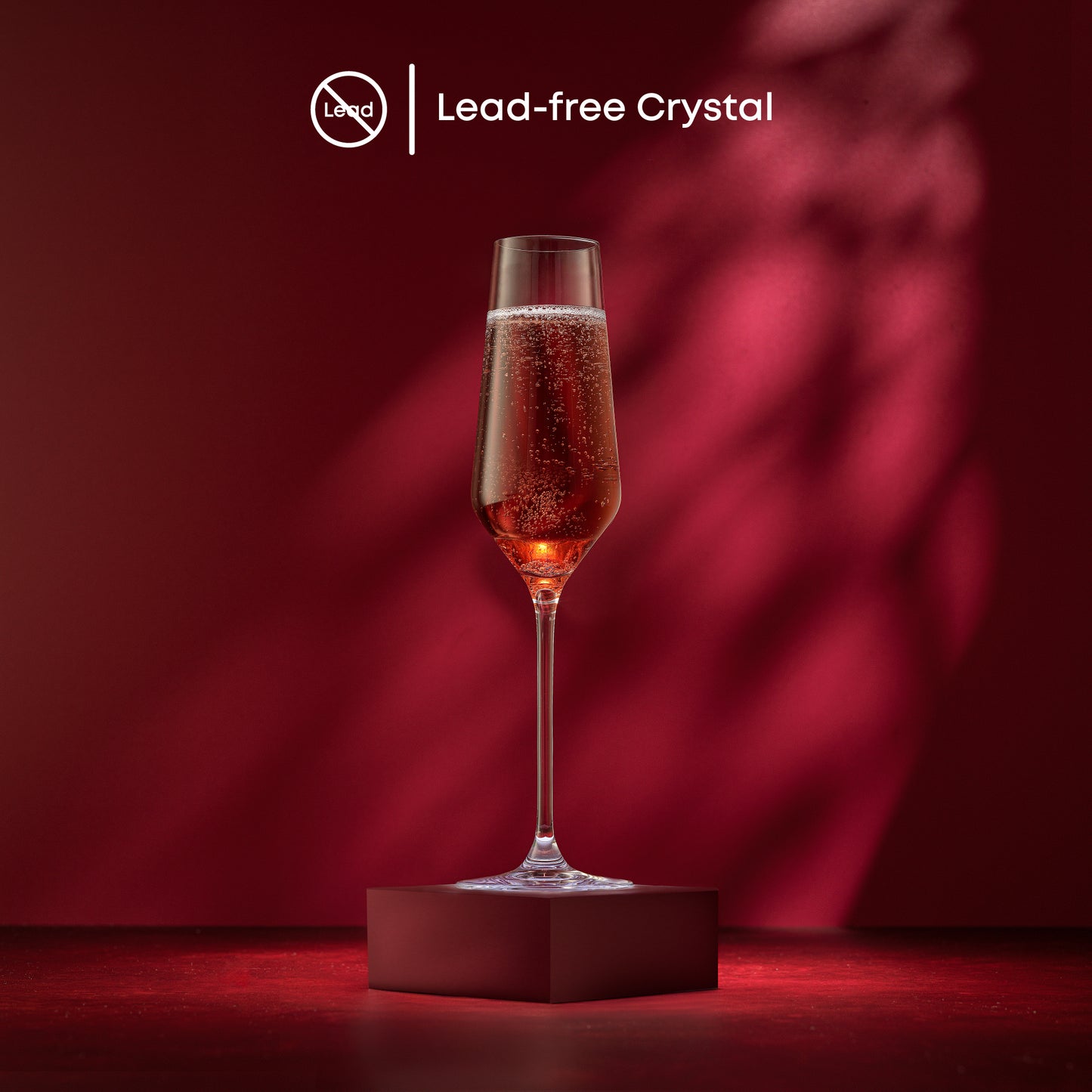 A champagne glass full of champagne on a red stand against a red background with text saying lead free crystal.