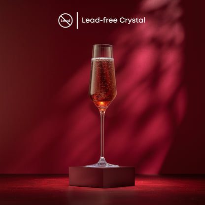 A champagne glass full of champagne on a red stand against a red background with text saying lead free crystal.