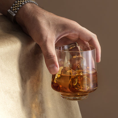 Hand holding a glass of whiskey with ice against a neutral background