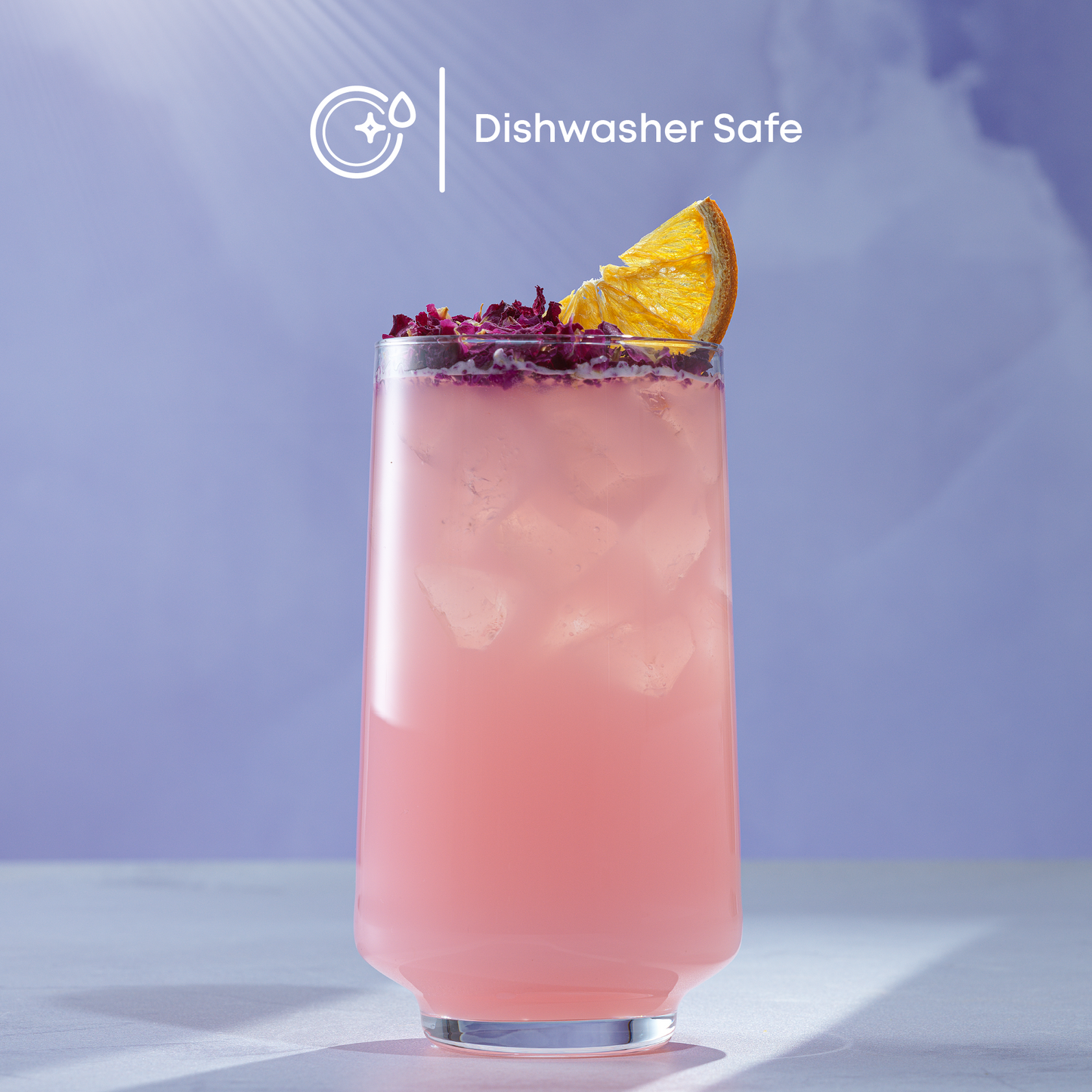Pink cocktail with lemon wedge and purple flowers in a tall glass on a light surface with a purple gradient background.