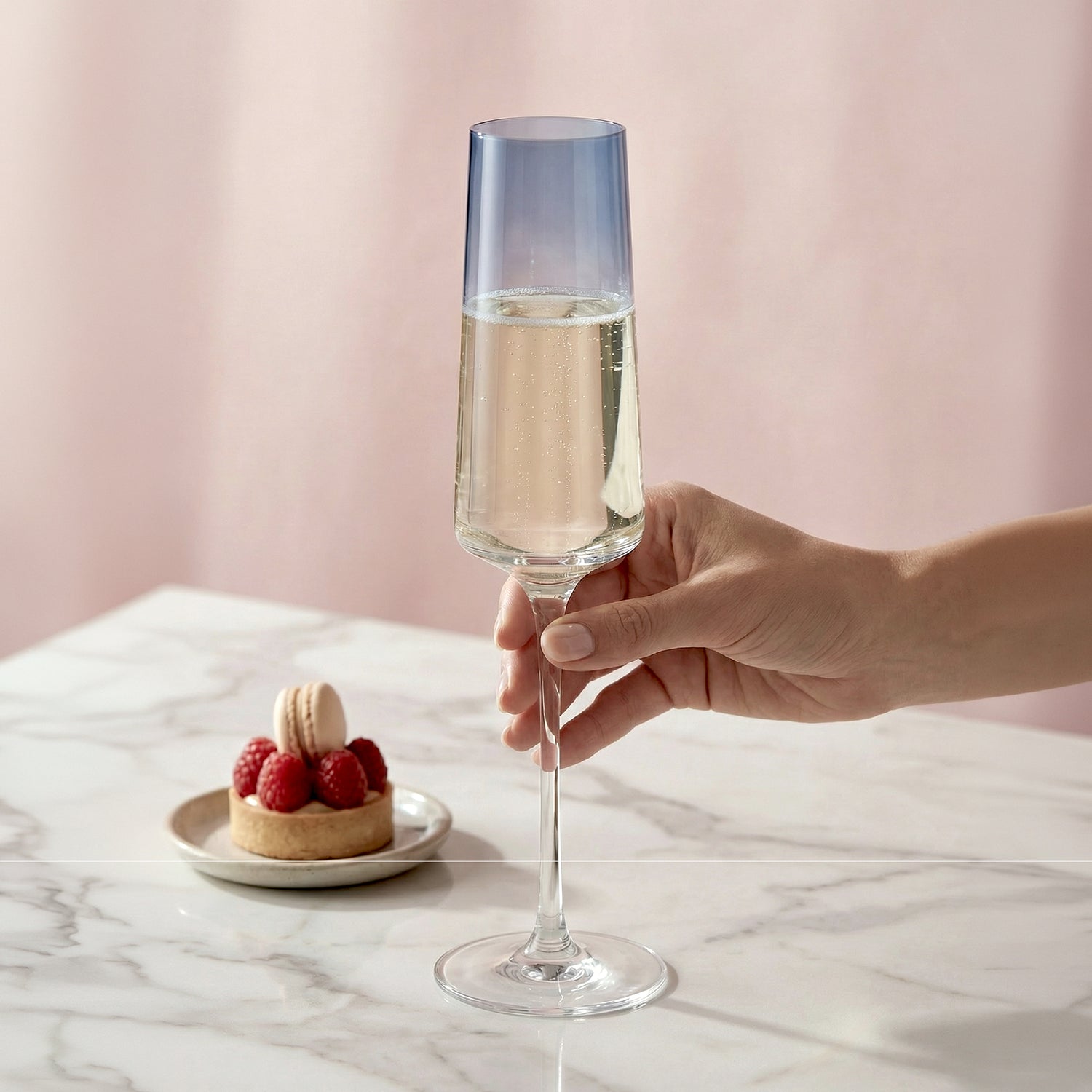 Hand holding a glass of champagne with a dessert on a marble surface