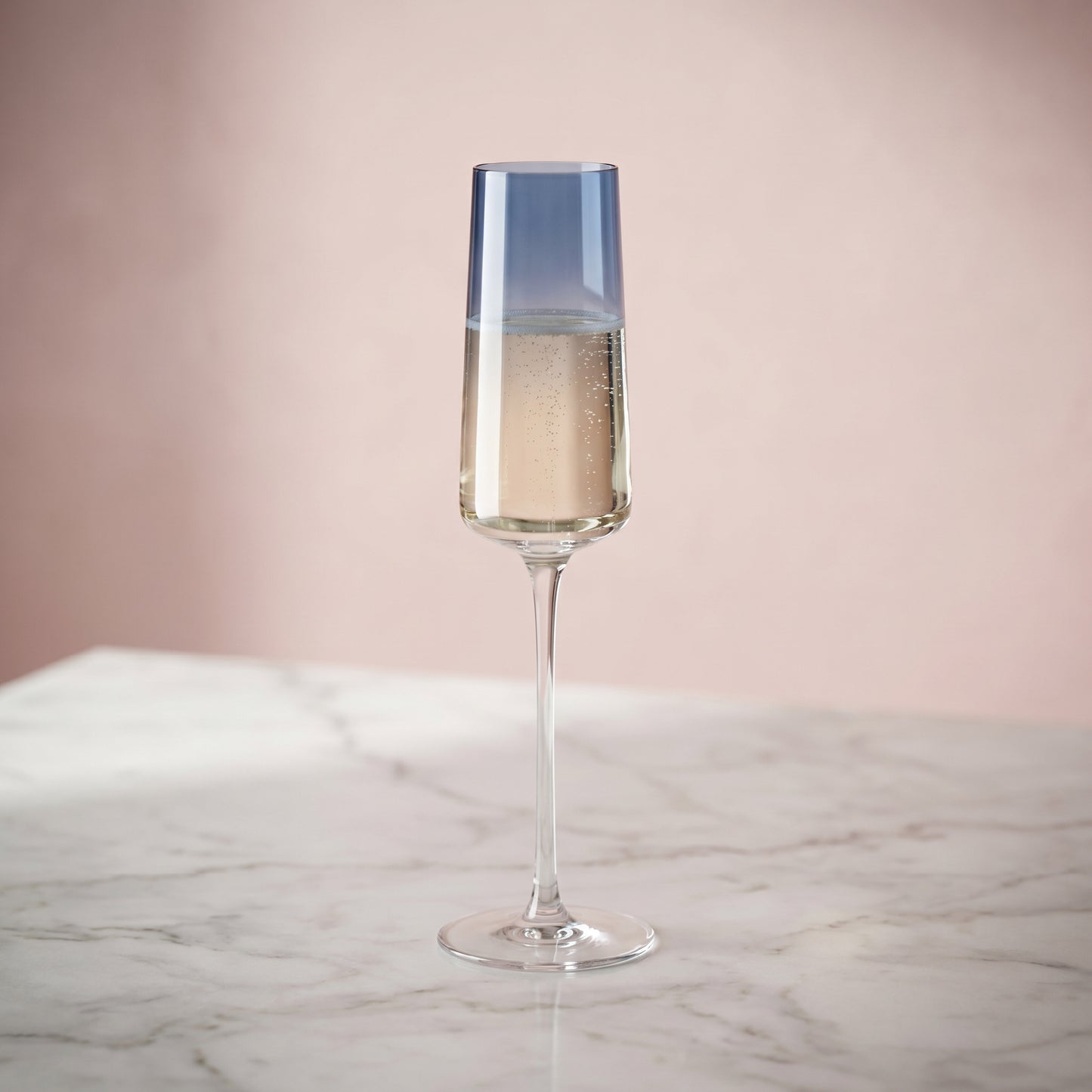 Champagne flute with a blue accent on a marble surface against a pink background