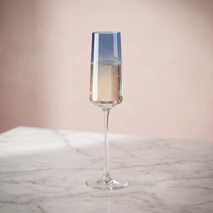 Champagne flute with a blue accent on a marble surface against a pink background