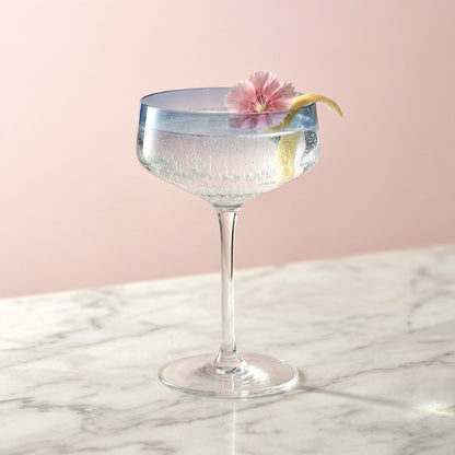 Cocktail in a glass with a pink flower and lemon twist on a marble surface with a pink background