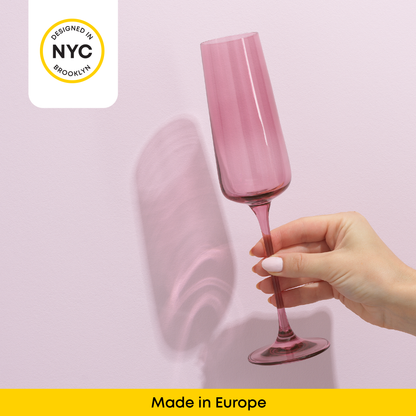 Pink champagne flute held by a hand against a light pink background with 'Designed in NYC' and 'Made in Europe' text.