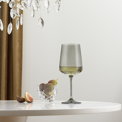 Wine glass and small bowl with figs on a table, with a chandelier in the background.