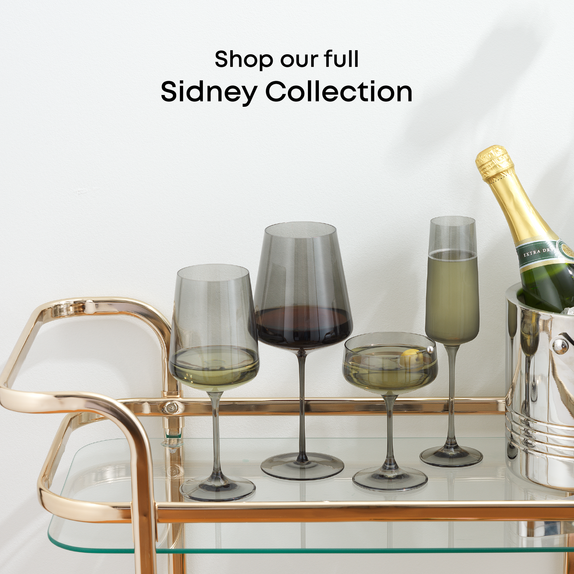 Stemmed glasses and a bottle on a bar cart with 'Shop our full Sidney Collection' text.