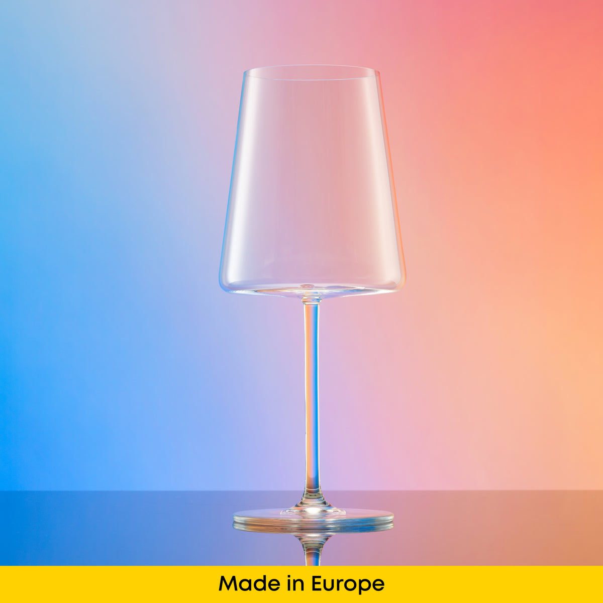 Made in Europe Aura wine glass with a contemporary tapered bowl and slender stem on a colorful reflective surface.