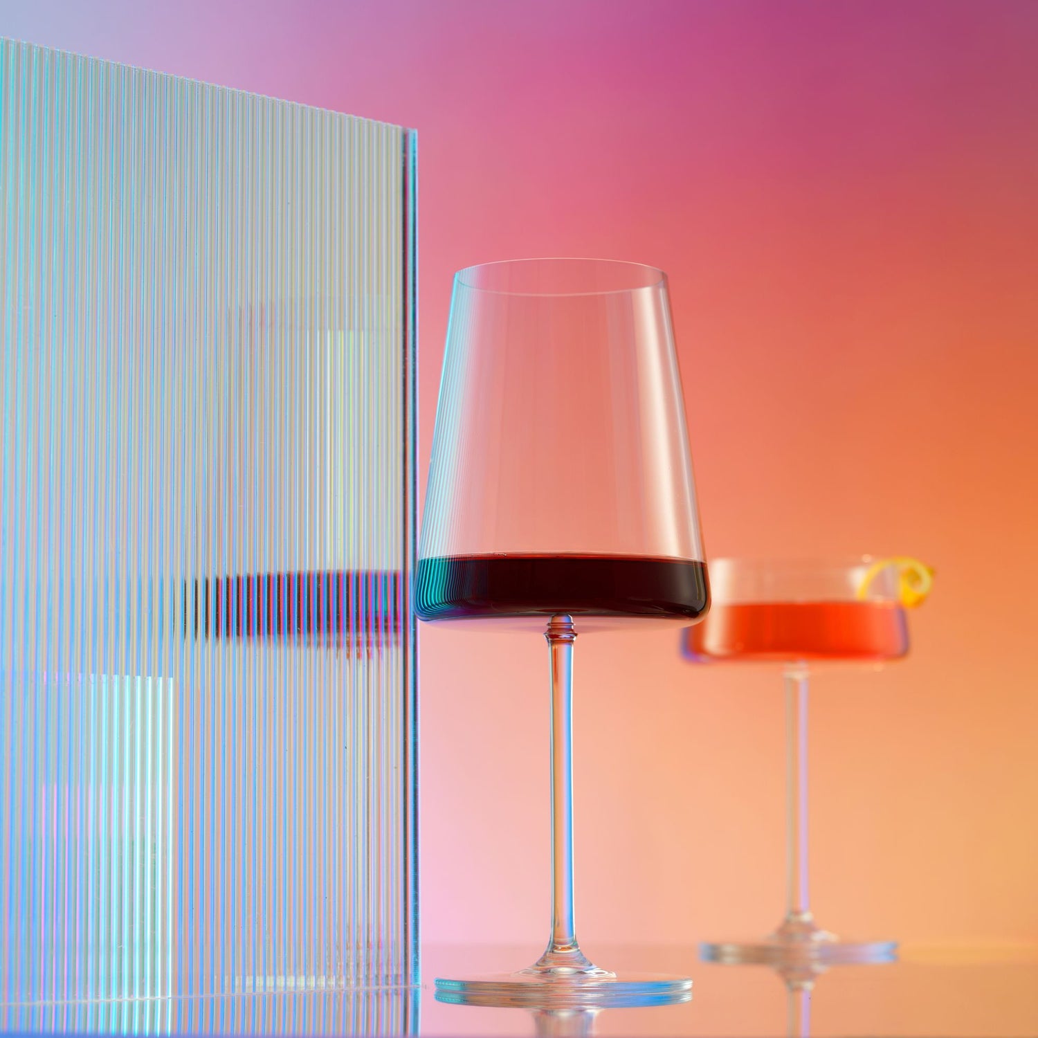 Two glasses, one with red wine and the other with a red beverage, against a colorful gradient background.