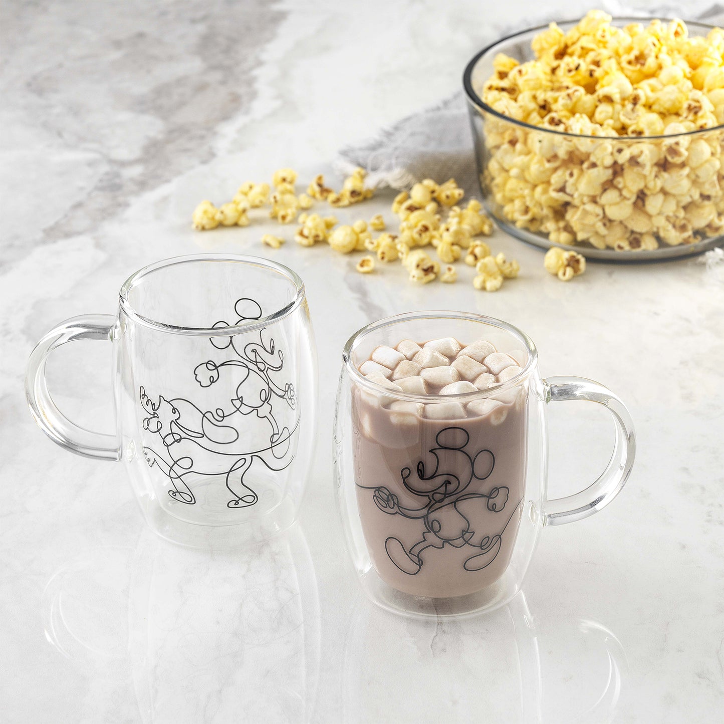 A mug full of hot cocoa topped with marshmallows sits on the counter next to a bowl of popcorn
