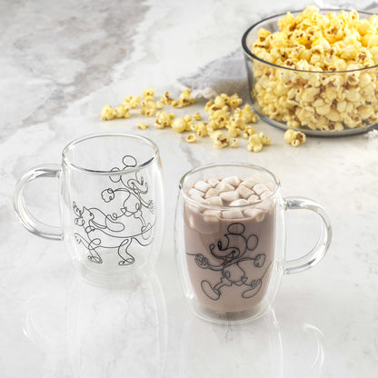 A mug full of hot cocoa topped with marshmallows sits on the counter next to a bowl of popcorn