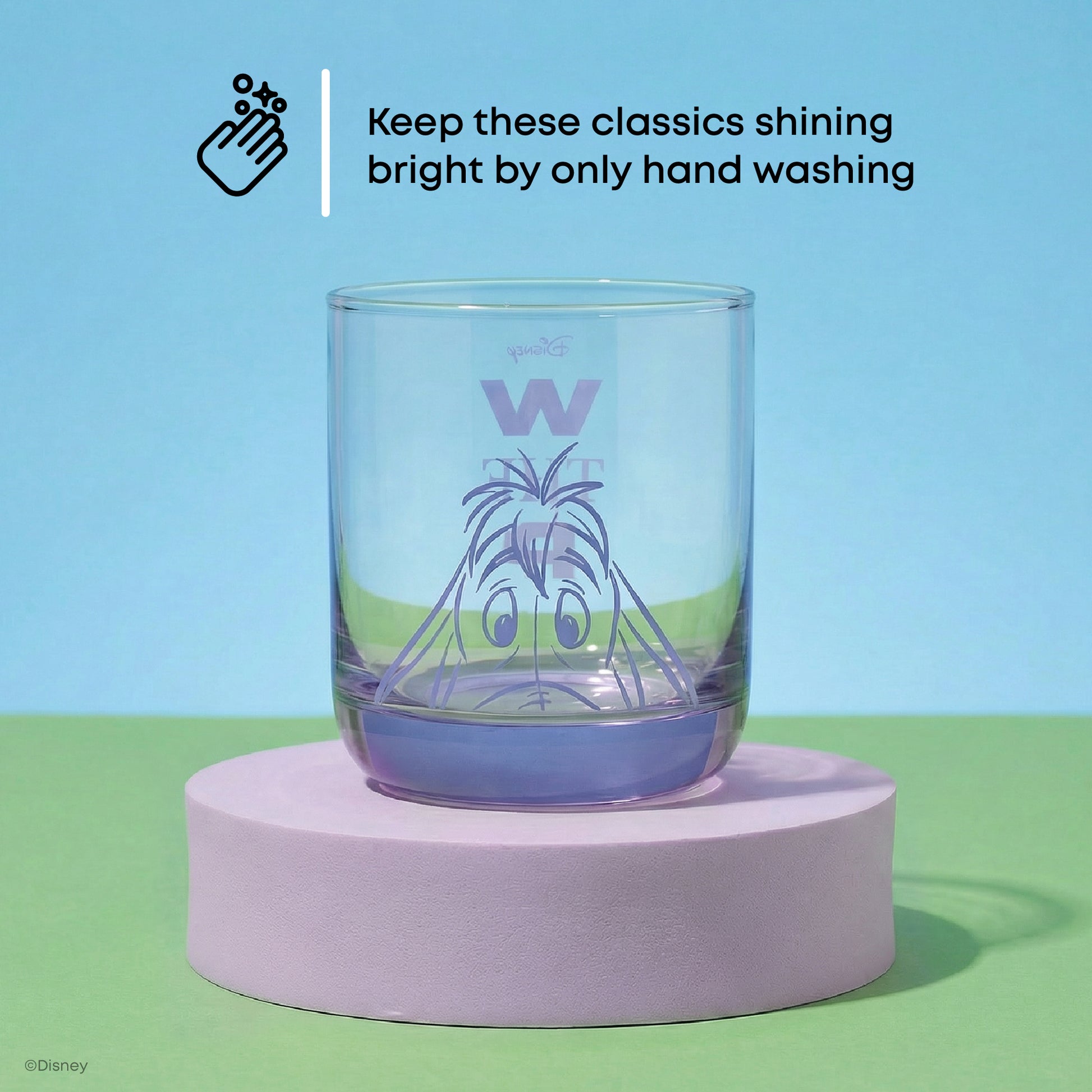 Clear glass with a character design of Eeyore in purple on a purple platform against a blue and green background with text: "keep these shining bright by only handwashing"