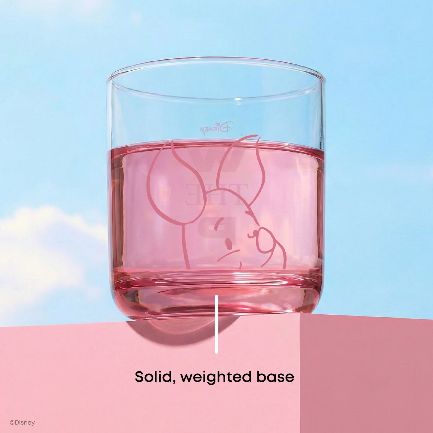 Glass with a character design of Piglet in pink filled with pink liquid on a blue and pink gradient background with text "solid, weighted base"