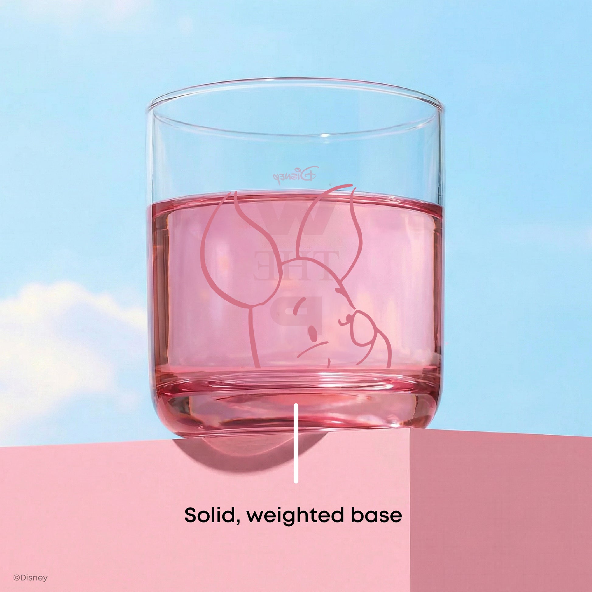 Glass with a character design of Piglet in pink filled with pink liquid on a blue and pink gradient background with text "solid, weighted base"