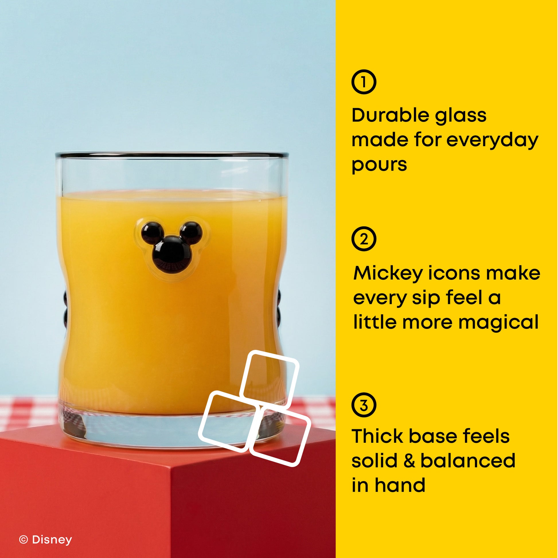 A Mickey Mouse-shaped clear glass tumbler filled with orange juice, shown on a red pedestal against a light blue background with a bright yellow text panel on the right describing product features. Disney branding appears in the lower left.