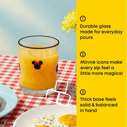 A Mickey Mouse-themed glass of orange juice on a red-and-white checkered tablecloth, with a bright yellow text panel on the right listing product features. The glass has a black rim and a black Mickey silhouette with a small red bow tie detail.