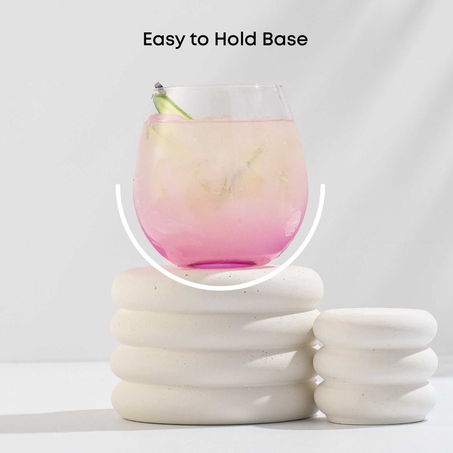 Pink stemless wine glass highlighting its stemless shape that is easy to hold on a white stand.