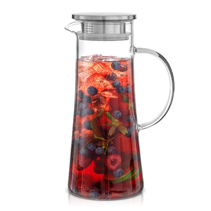 Clear glass pitcher and stainless steel lid filled with a red berry drink mixture on a white background