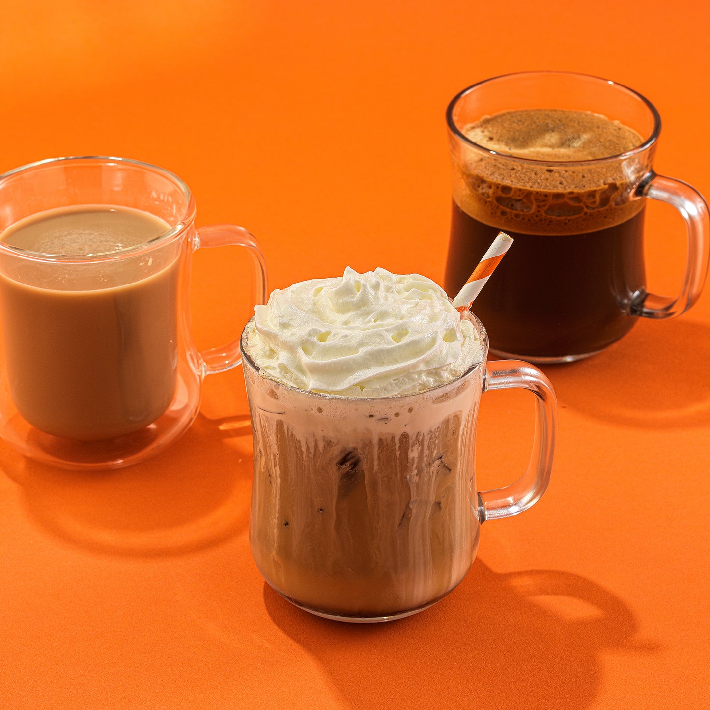 Three glass mugs with different beverages on an orange background