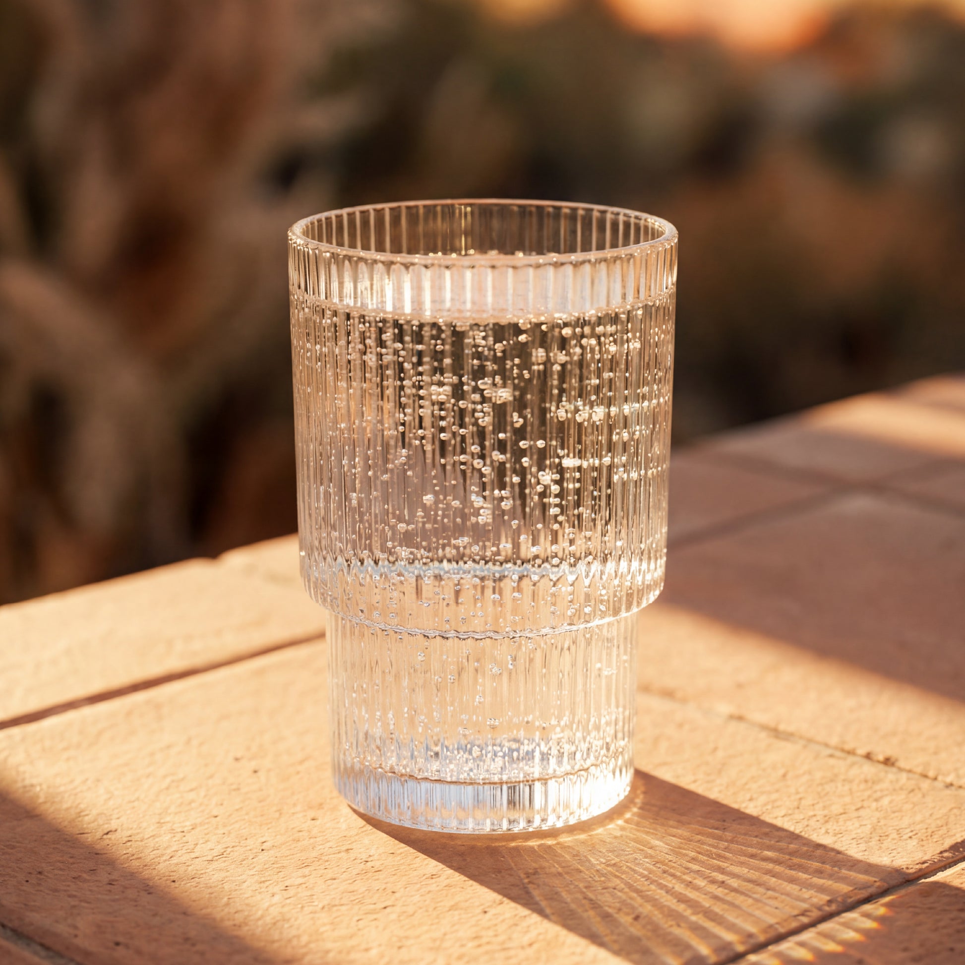 Clear textured glass on a wooden surface with a blurred natural background