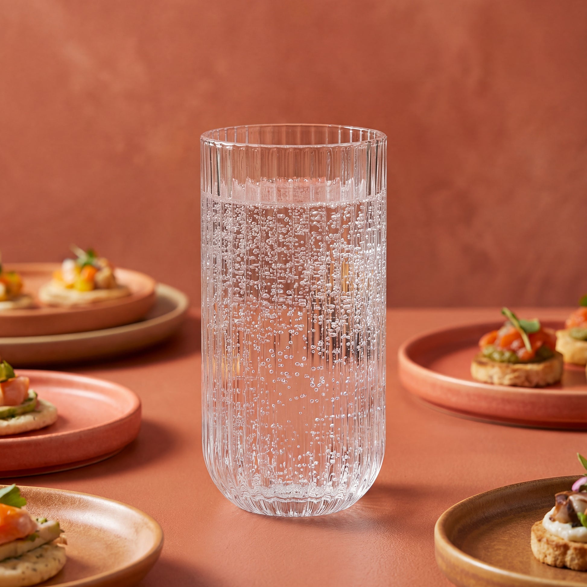 Clear textured glass on a pink surface with plates of food in the background