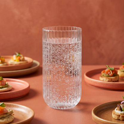 Clear textured glass on a pink surface with plates of food in the background