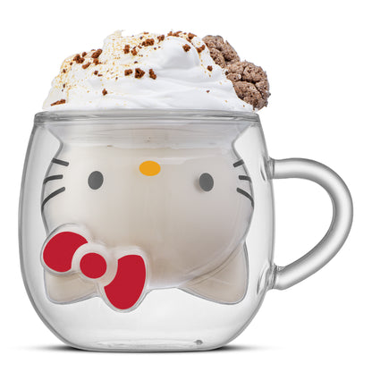 Clear glass mug with a 3D design of Hello Kitty's face upside down, filled with a drink and topped with whipped cream and a dessert, on a white background