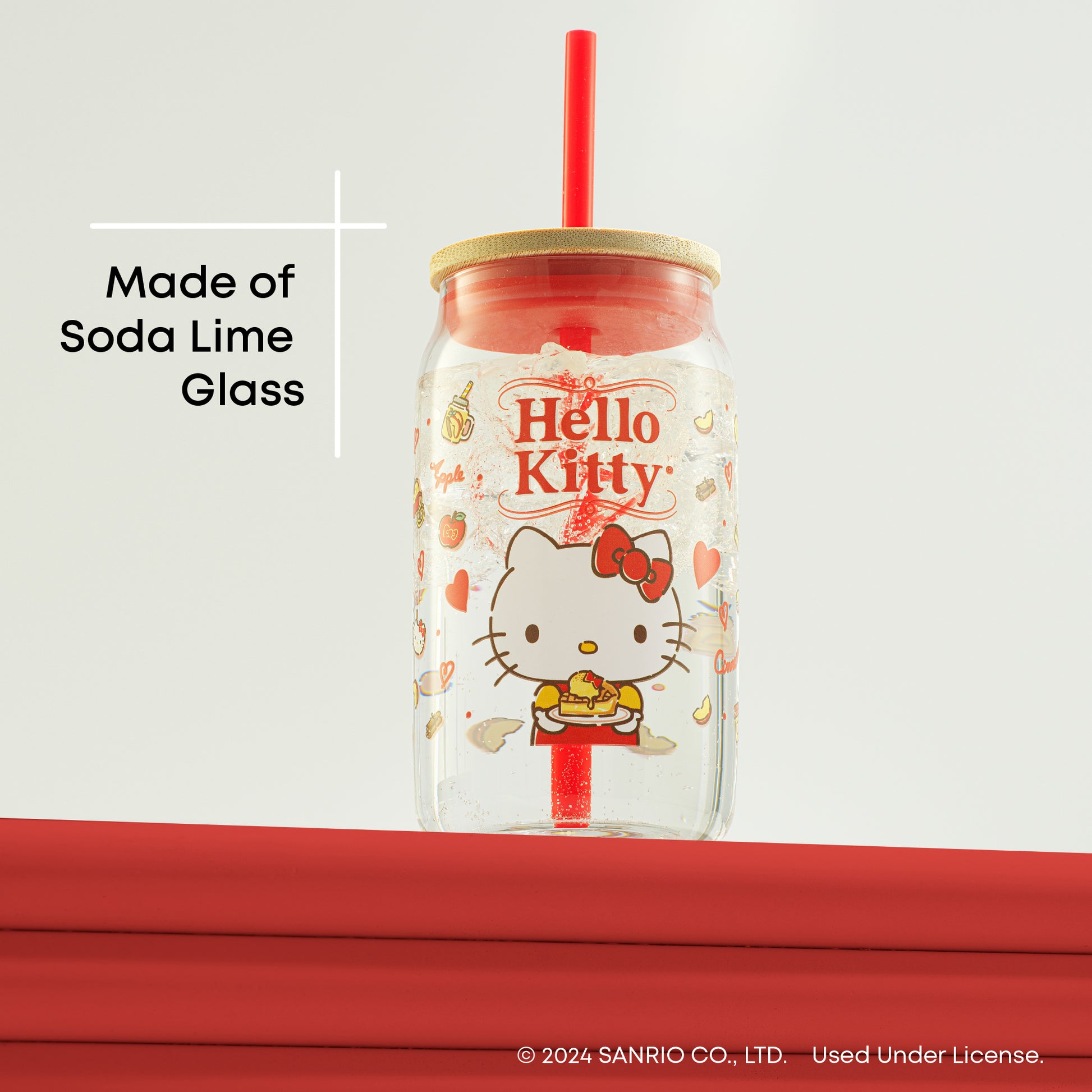A Hello Kitty glass tumbler with a straw. The tumbler is made of clear soda lime glass and features a red bow and Hello Kitty’s face printed on it. There is text on the image that says “Made of Soda Lime Glass.”