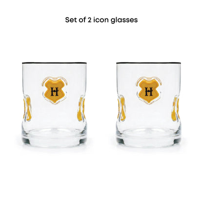Set of 2 clear glass icon tumblers with a gold crest design featuring a black letter 'H' on a white background, with black text above reading 'Set of 2 icon glasses'.