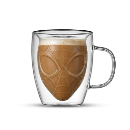 A clear double-walled glass mug with a Spider-Man mask design printed inside, filled with a brown coffee drink and photographed on a white background.