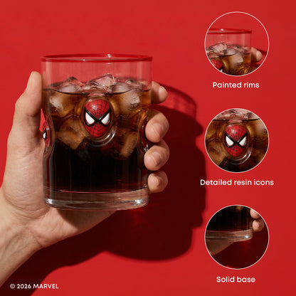 A hand holds a clear glass tumbler with a Spider-Man face design in the center, filled with a dark cola-colored drink and ice cubes, against a solid red background. Three circular inset callouts on the right highlight product features: painted rims, detailed resin icons, and a solid base.