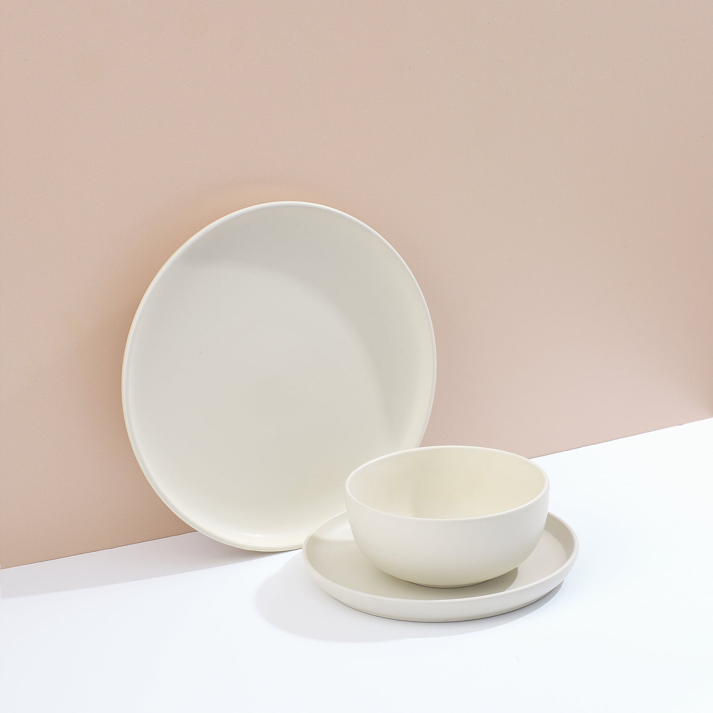 Set of white dinnerware including bowls and plates on a white surface and muted pink background.