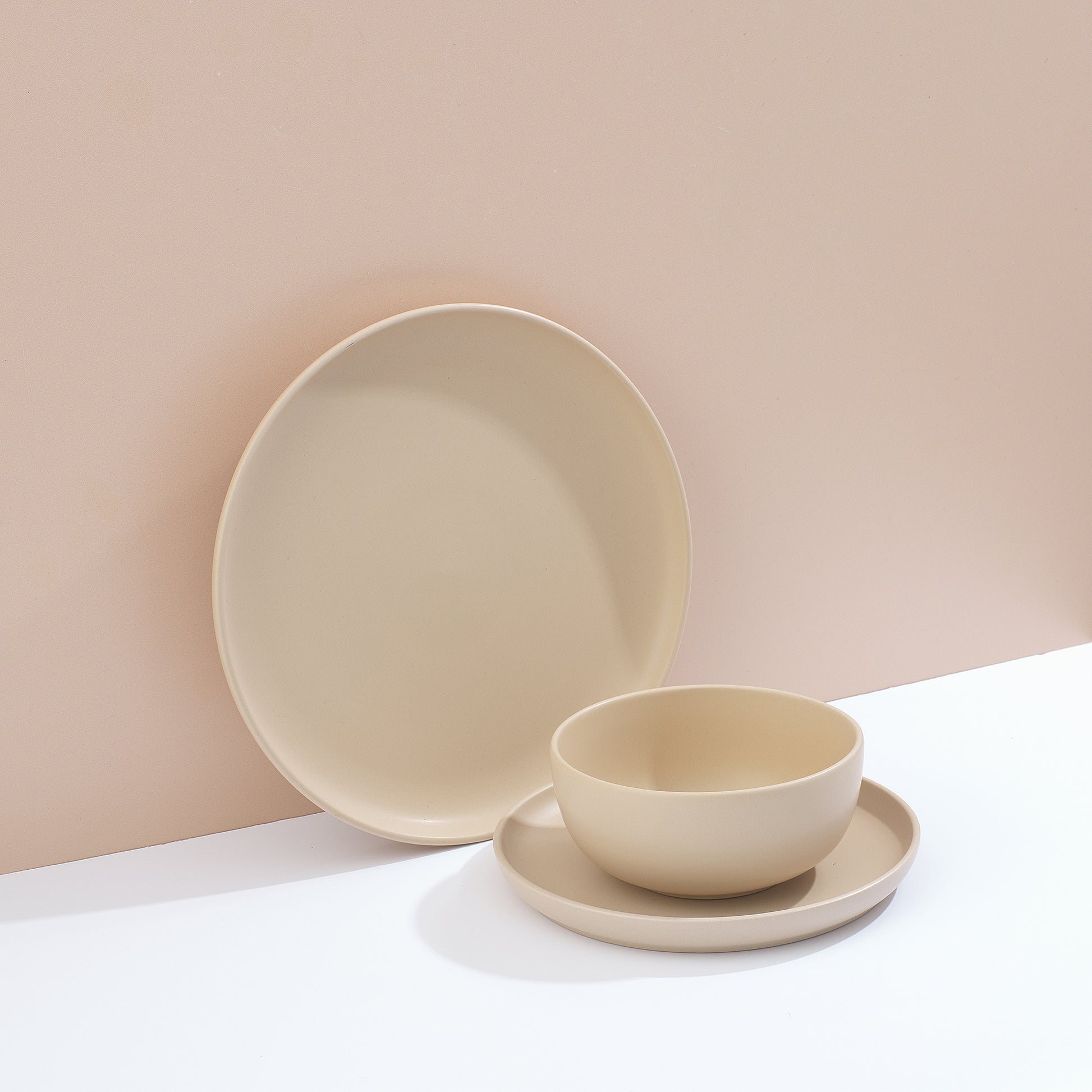 Set of beige dinnerware including bowls and plates on a white surface and muted pink background.