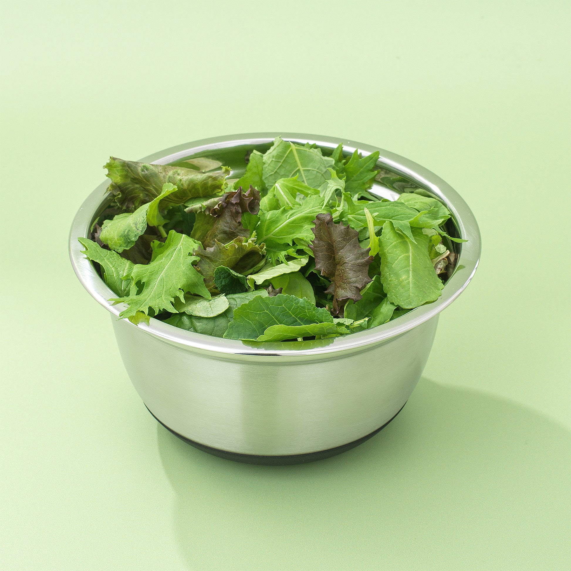 A stainless steel bowl with leafy greens inside it, to the brim, against a green background.