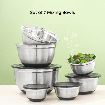 Set of stainless steel mixing bowls with black lids on a white surface with green background. Medium-small size bowl contains a salad. With text " set of 7 mixing bowls."