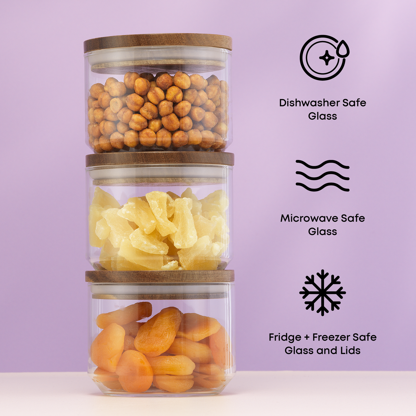 Stack of glass containers with wooden lids, filled with snacks, on a light purple background. with text: "dishwasher and microwave safe glass, fridge and freezer safe glass and lids"