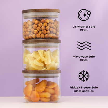 Stack of glass containers with wooden lids, filled with snacks, on a light purple background. with text: "dishwasher and microwave safe glass, fridge and freezer safe glass and lids"