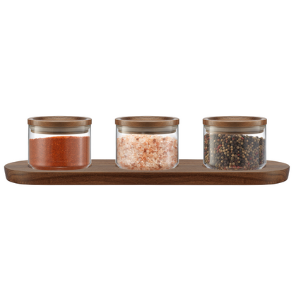 Set of three glass canisters with wooden lids on a wooden tray against a white background