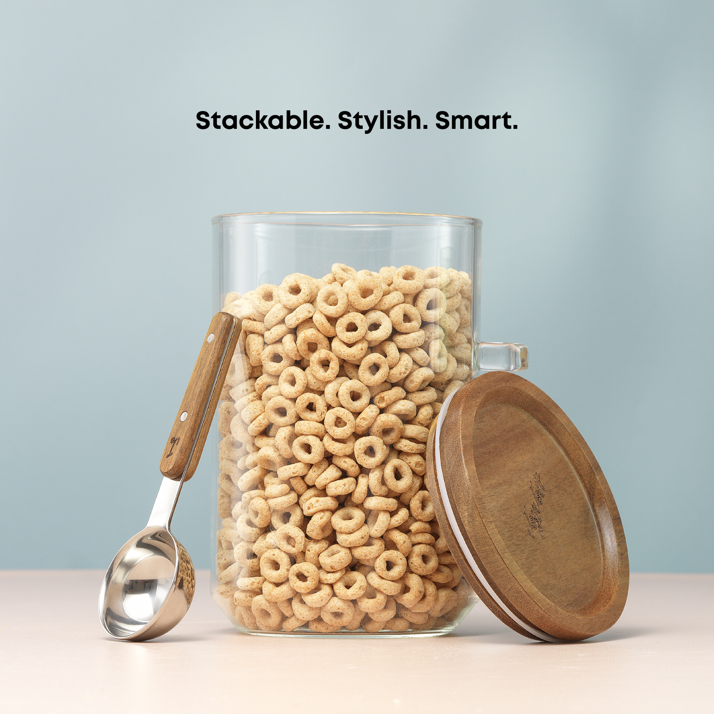 Glass canister with wooden lid and spoon filled with cereal, on a light blue background.