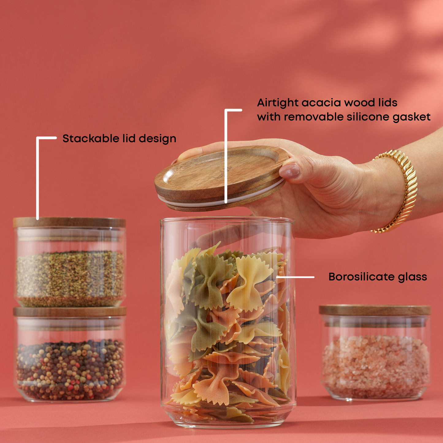 Glass storage jars with wooden lids, filled with various foods, on a red background. With text: "borosilicate glass, stackable lid design, airtight acacia wood lids with removable silicone gasket"